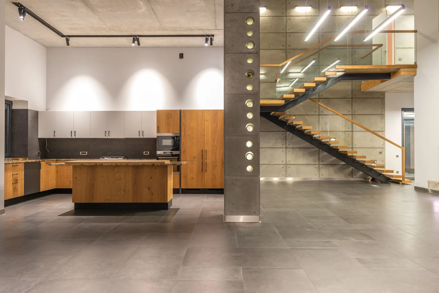 Intérieur contemporain associant béton apparent, cuisine en bois et escalier suspendu, photographié par Max Vakhtbovych.