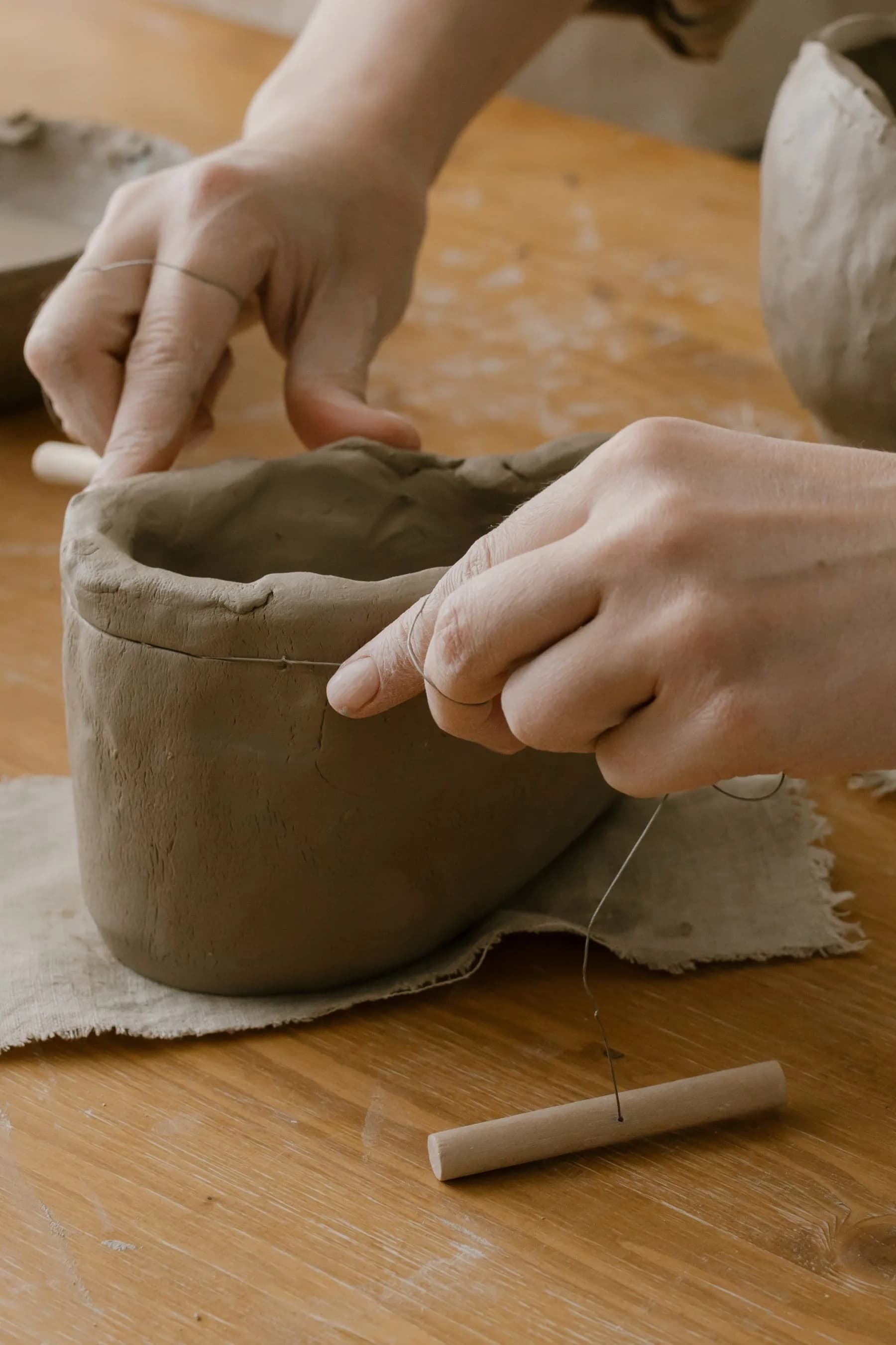 Gros plan sur des mains façonnant une pièce d’argile avec un outil, dans un atelier de poterie.